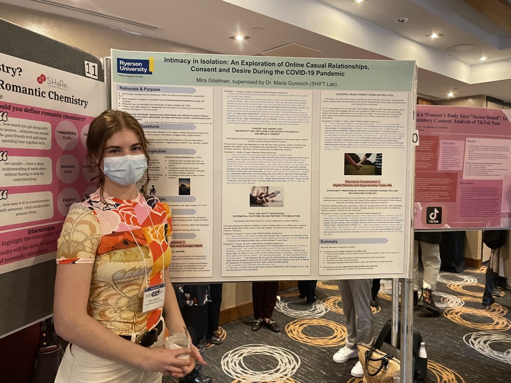 A young woman smiling and standing beside an "Intimacy in isolation" poster at the Canadian Sex Research Forum conference.